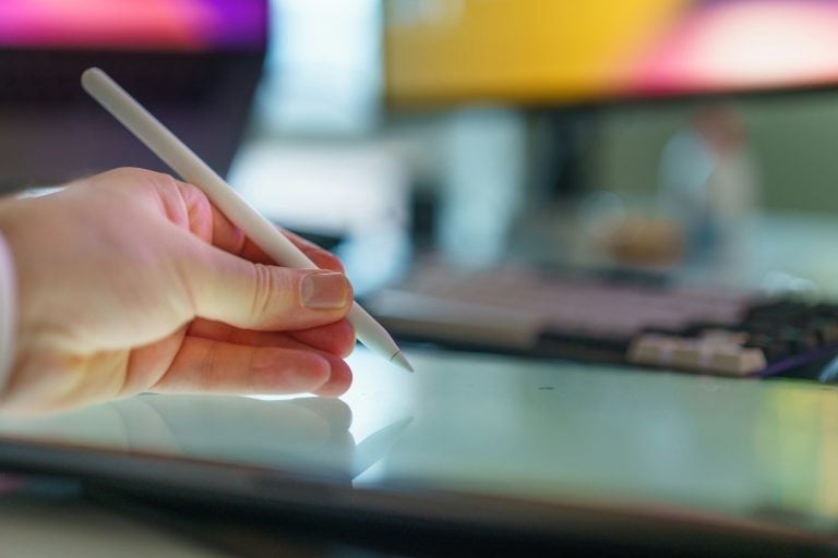 A hand holds a stylus above a tablet.