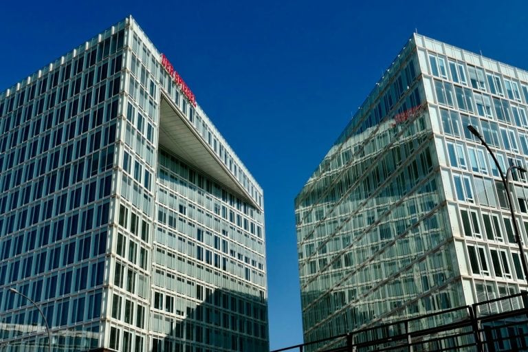 Modern high-rise buildings stand against a bright blue sky.